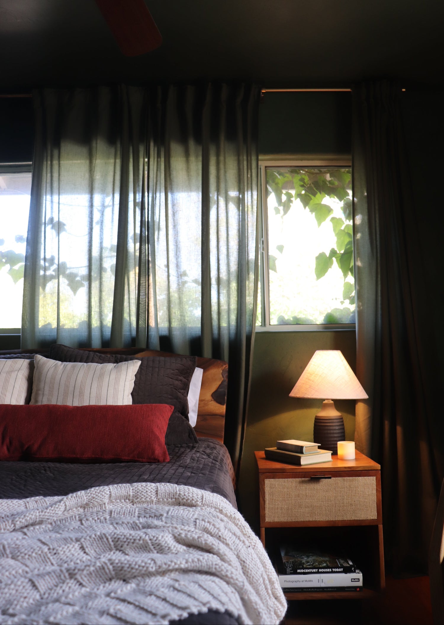 A dark charcoal gray curtain panel with a subtle horizontal striped pattern, shown hanging in front of a window in a cozy bedroom setting.