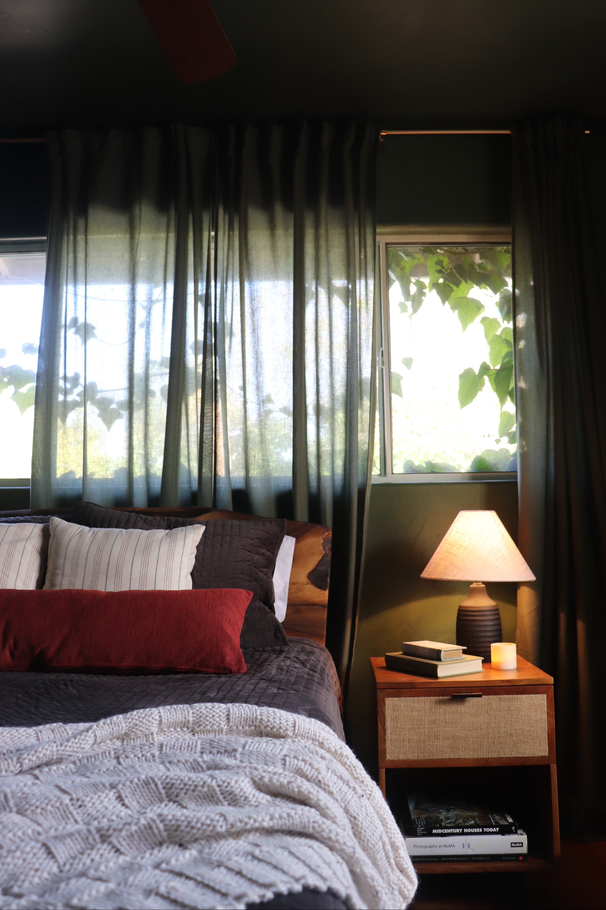 A dark charcoal gray curtain panel with a subtle horizontal striped pattern, shown hanging in front of a window in a cozy bedroom setting.