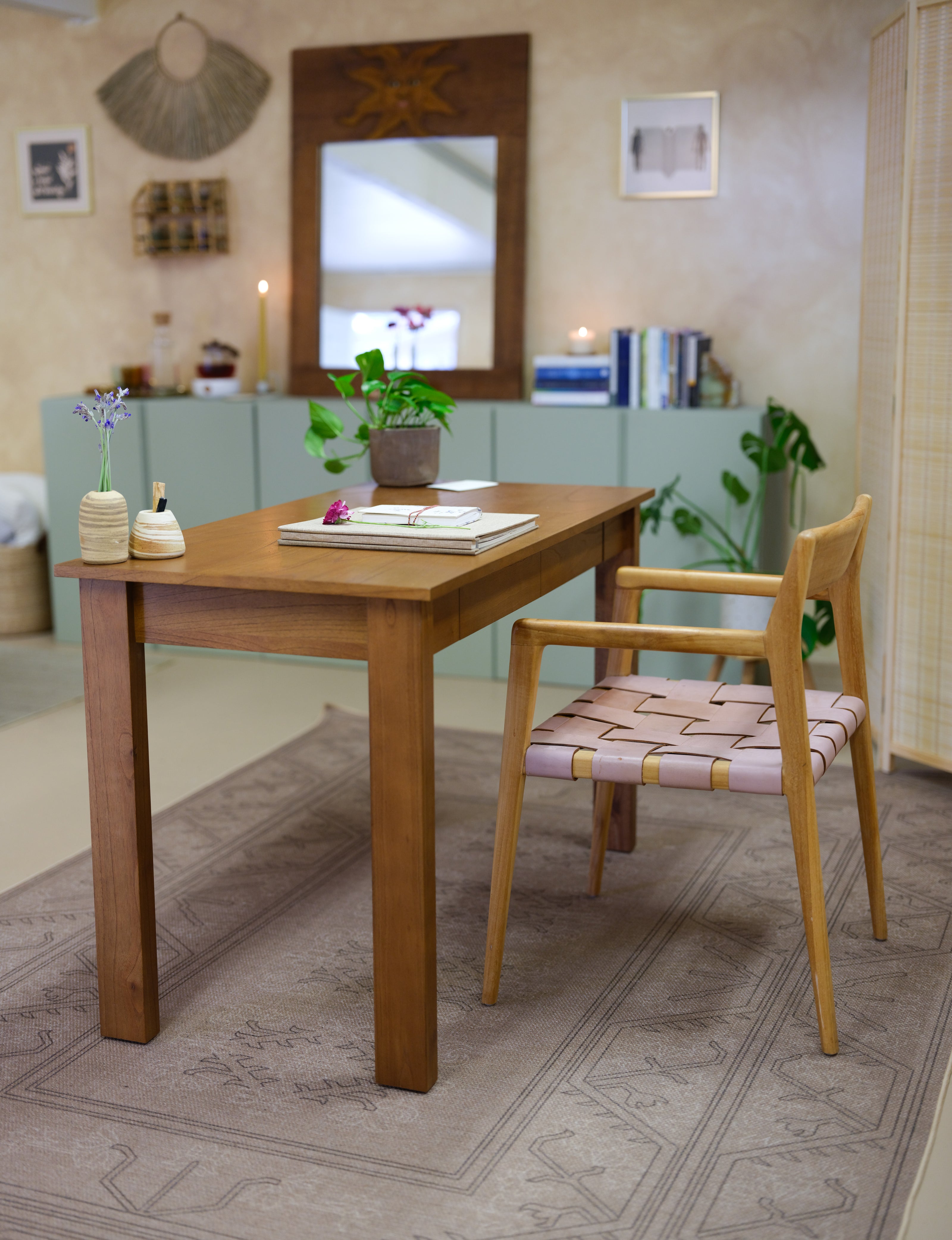 A wooden dining table with a wooden armchair featuring a pink and beige woven seat, set on a patterned area rug in a styled home interior.